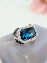 bague cocktail centrée d'une topaze facetée serti clos entourée de petits diamants et de saphirs sur le panier or 750 millième (18