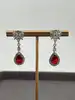 boucles d'oreilles pendantes chacune centrée d'une pierre rouge entouré d'oxydes